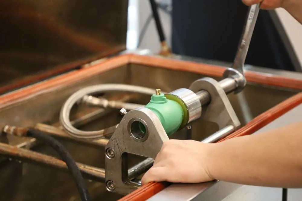 Green PP-R valve body clamped between metal test fixtures over a tank